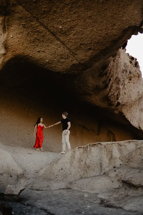 Pareja bailando en vestido rojo bajo bóveda natural de arco de roca en Tenerife