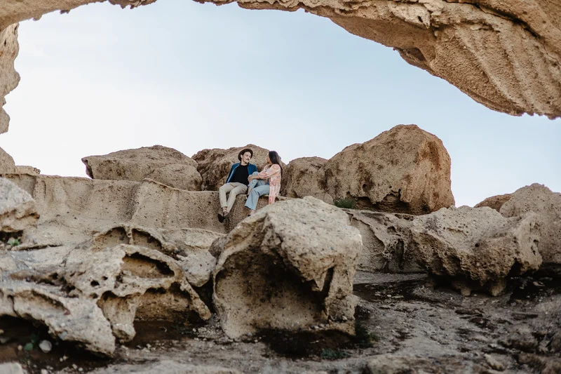Couple embracing under massive rock arch with view of Tenerife volcanic formations