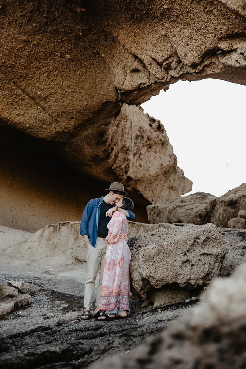 Elegant couple in pink dress and hat under monumental rock arch during golden hour