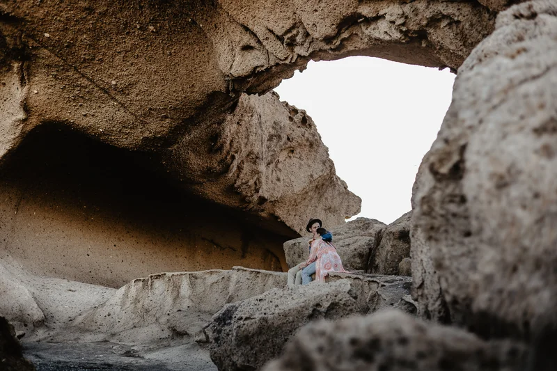 Loving couple under natural stone arch in golden light during engagement session