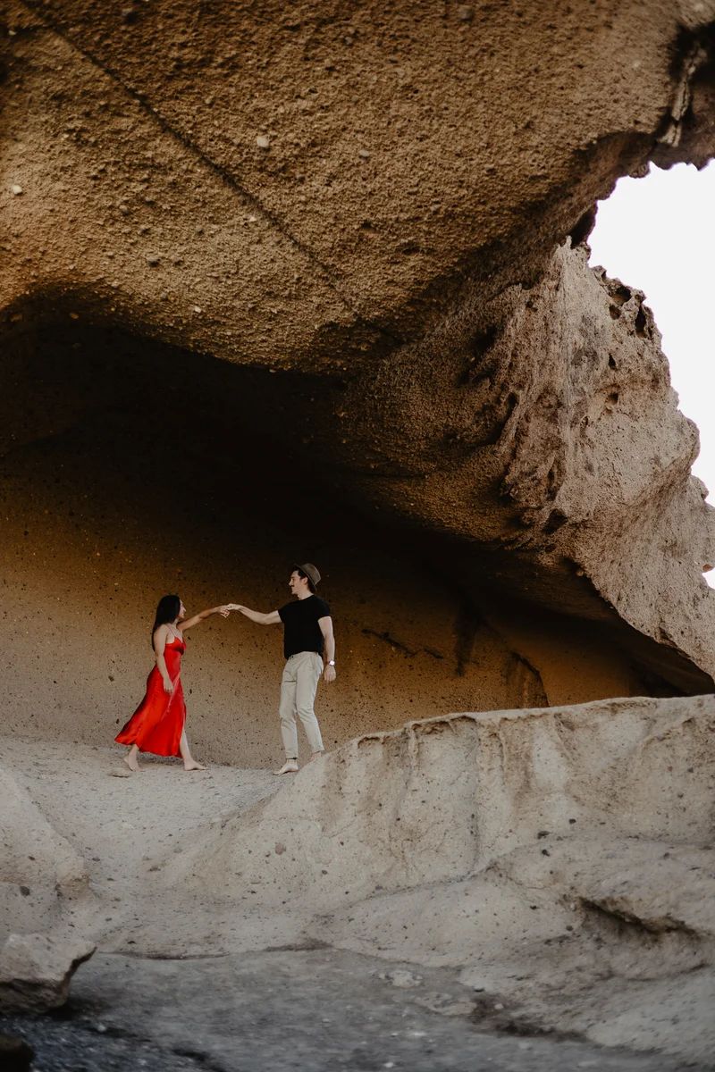 Couple's dance in red dress under rock arch in dramatic natural light