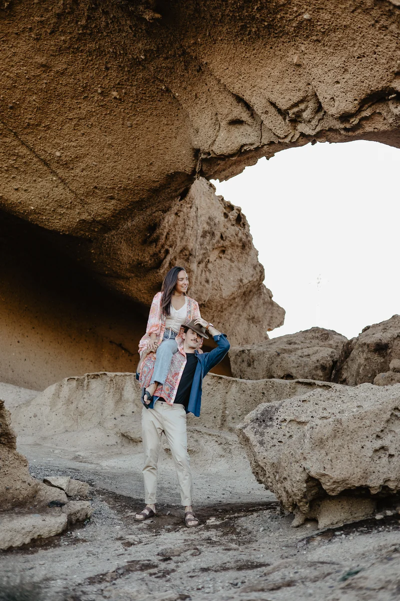 Man lifting partner under massive rock arch in joyful moment of photo session