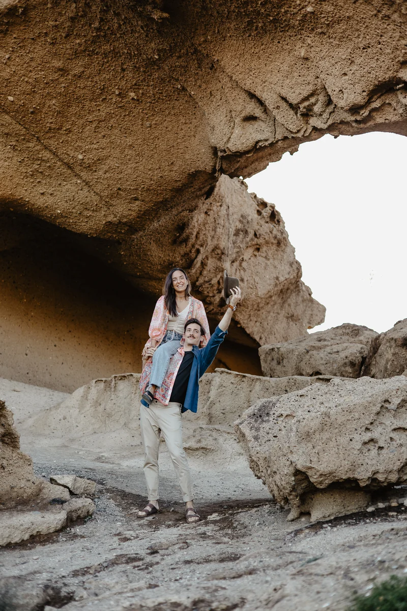 Stylish couple posing under rock arch in blue-pink styling against desert landscape background
