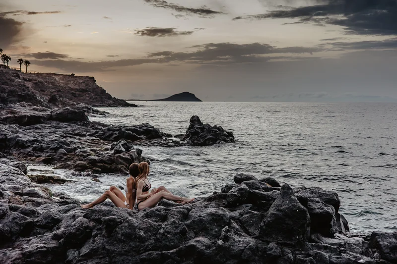 Modelos en bikini en las rocas volcánicas negras de Tenerife durante la suave iluminación de la hora dorada