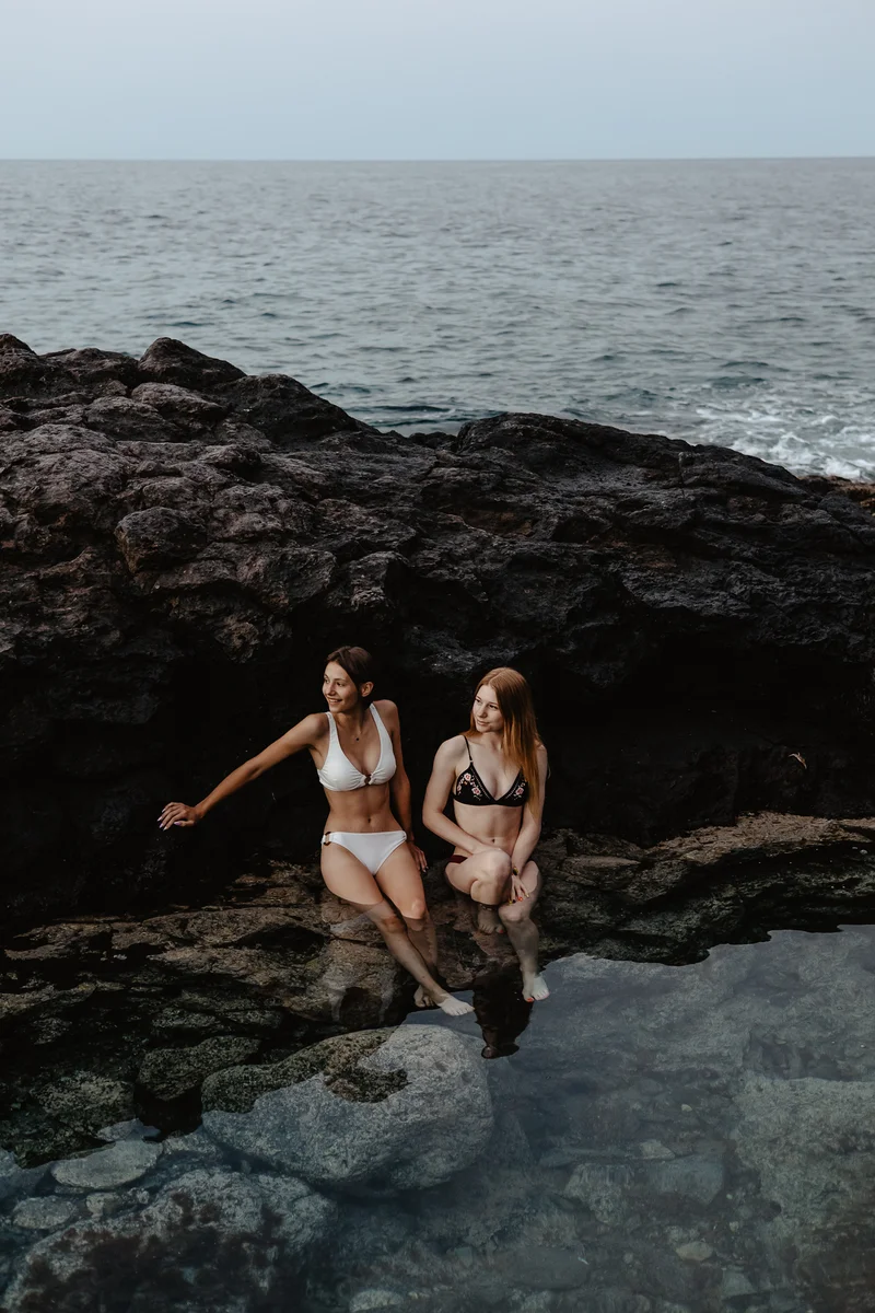 Piscinas naturales en las rocas volcánicas de Tenerife con dos mujeres en bikini bajo luz cálida