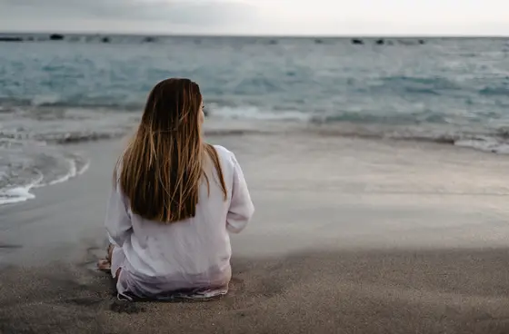 Pregnant woman sitting with back turned on sandy beach looking at ocean