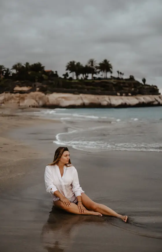 Pregnant woman in white shirt sitting on beach at sunset in Tenerife