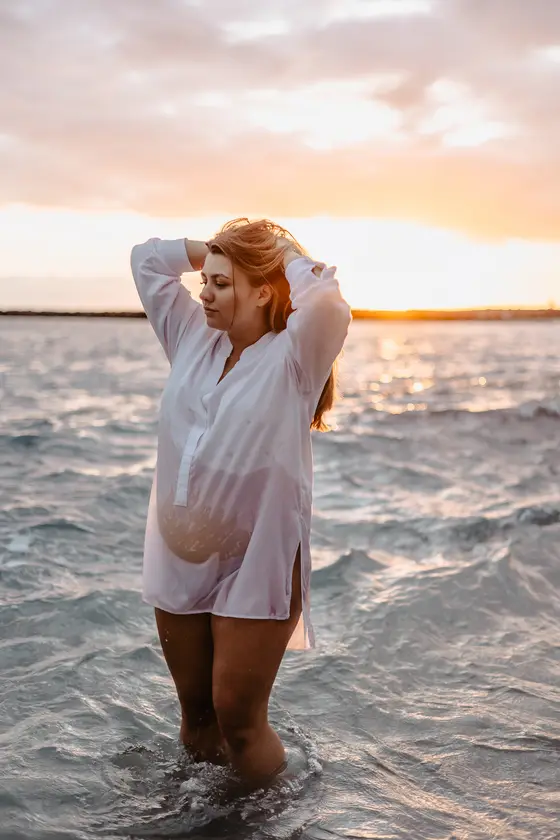 Golden hour maternity session - woman with hands in hair standing in ocean
