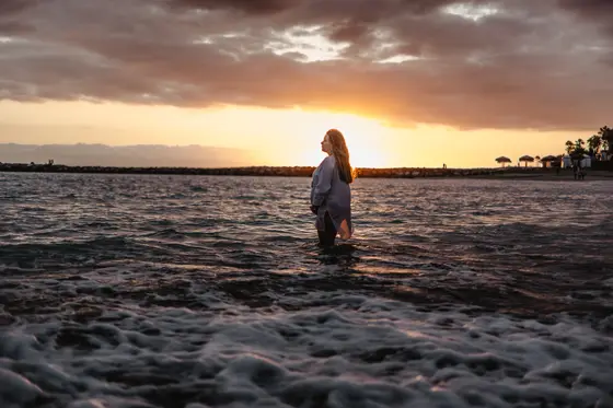 Pregnant woman standing in ocean during sunset in Tenerife wearing white dress