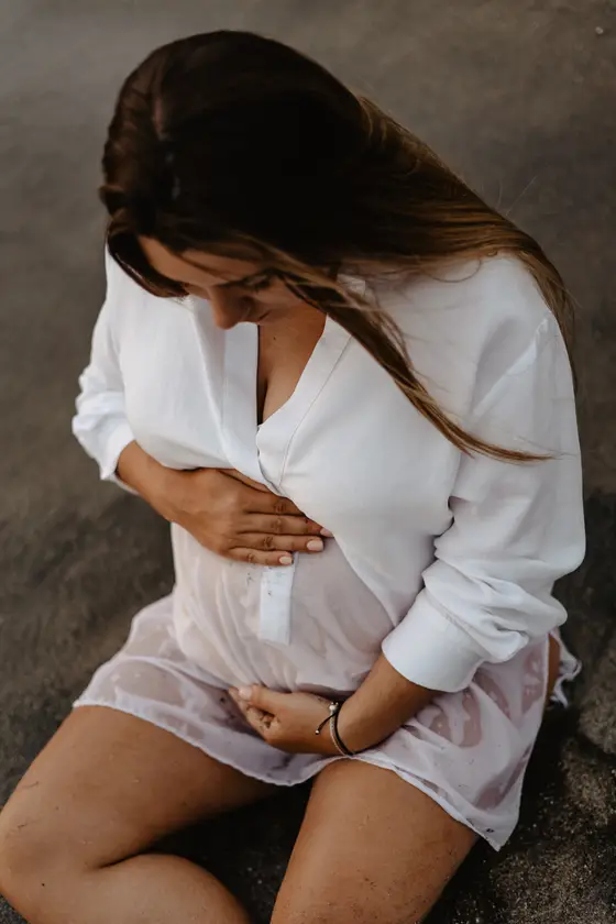 Intimate portrait of pregnant woman holding belly on beach at sunset