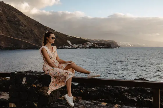 Mujer con gafas de sol sentada en plataforma de madera sobre el océano en Tenerife