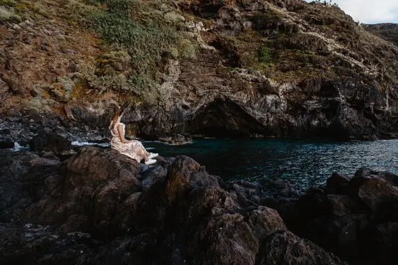 Mujer sentada en rocas volcánicas junto a piscina natural de agua turquesa en Tenerife