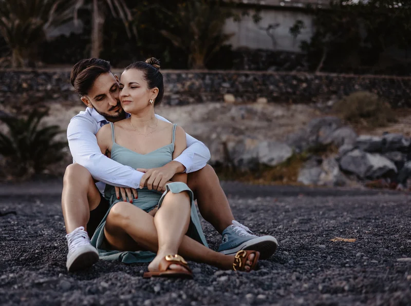 Elegante pareja española posando en costa rocosa de Tenerife con luz dorada del atardecer