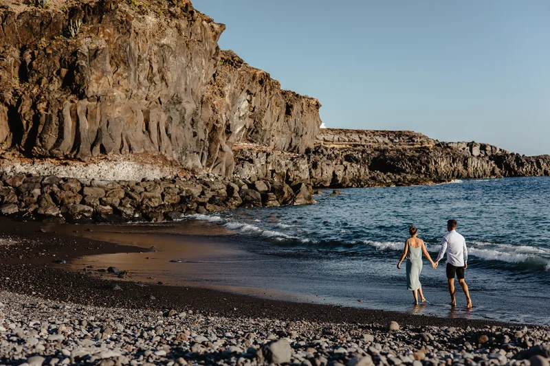 Pareja española caminando de la mano en dramática playa con acantilados en Tenerife