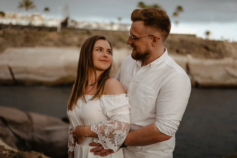 Beso íntimo de pareja comprometida en costa de Tenerife con palmeras y océano