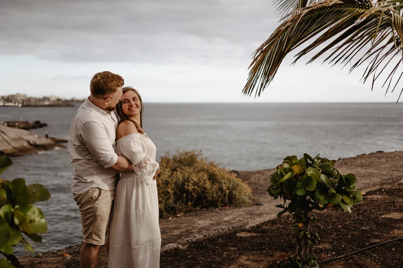 Pareja romántica comprometida junto al océano en Tenerife rodeada de palmeras y vegetación tropical