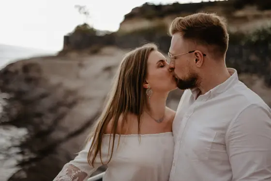 Beso romántico de pareja junto al océano contra fondo de costa rocosa de Tenerife