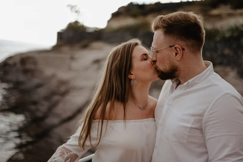 Beso romántico de pareja junto al océano contra fondo de costa rocosa de Tenerife