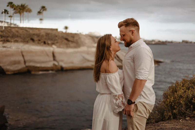 Pareja enamorada junto al océano en Tenerife con palmeras y costa rocosa de fondo