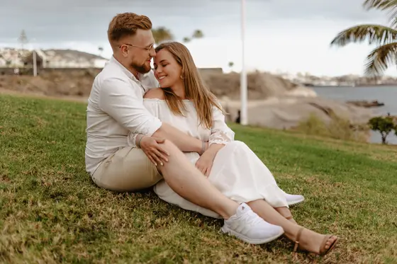 Pareja romántica sentada en césped durante sesión de compromiso en Tenerife con palmeras de fondo