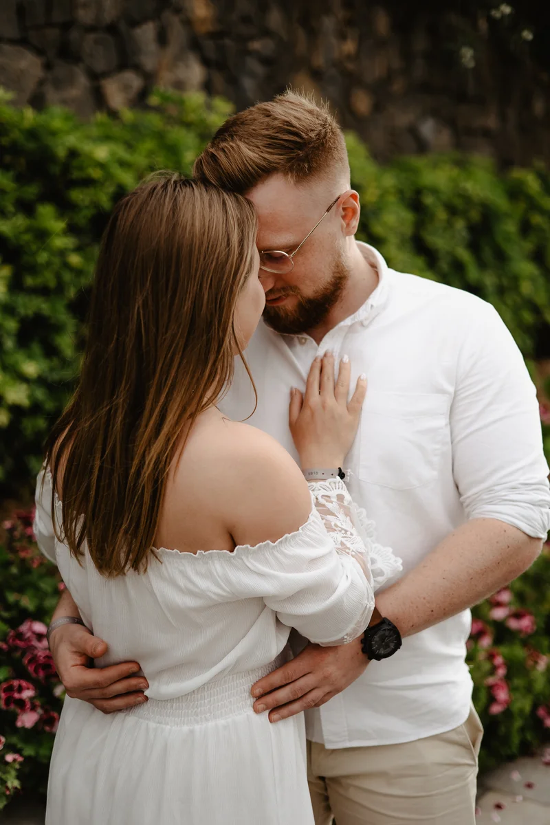 Momento tierno de pareja comprometida en jardín tropical de Tenerife con flores coloridas