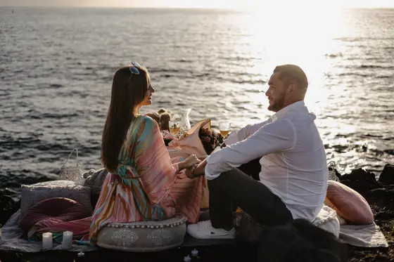 Brindis romántico con champán durante propuesta de picnic en playa de Tenerife en luz dorada