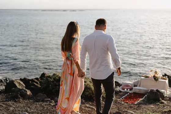 Pareja comprometida caminando de la mano junto al océano durante sesión fotográfica Tenerife