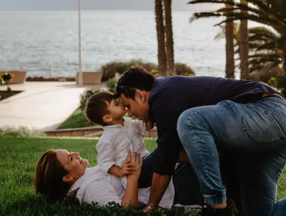 Intimate family moment on grass with palm trees backdrop during family photography Tenerife session
