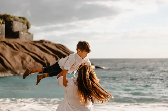 Mother spinning her son against rocky coastline backdrop during family photography Tenerife session