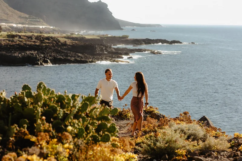 Pareja tomada de la mano en un acantilado con vistas al océano