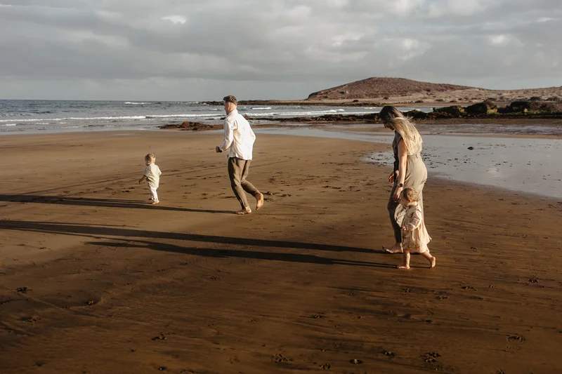 Familia corriendo por playa Tenerife sesión familiar vacaciones recreación activa montañas fondo