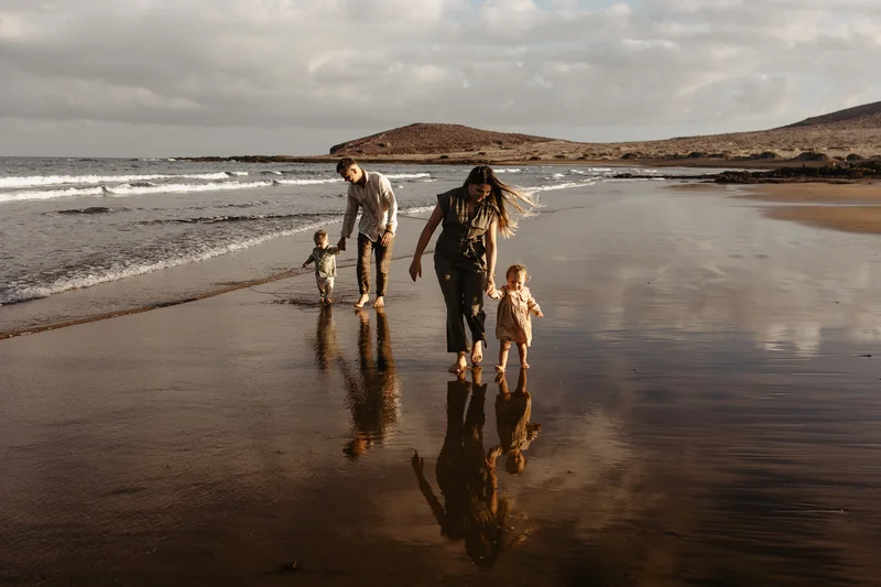 Familia caminando por playa Tenerife sesión familiar vacaciones reflejos agua recuerdos alegres