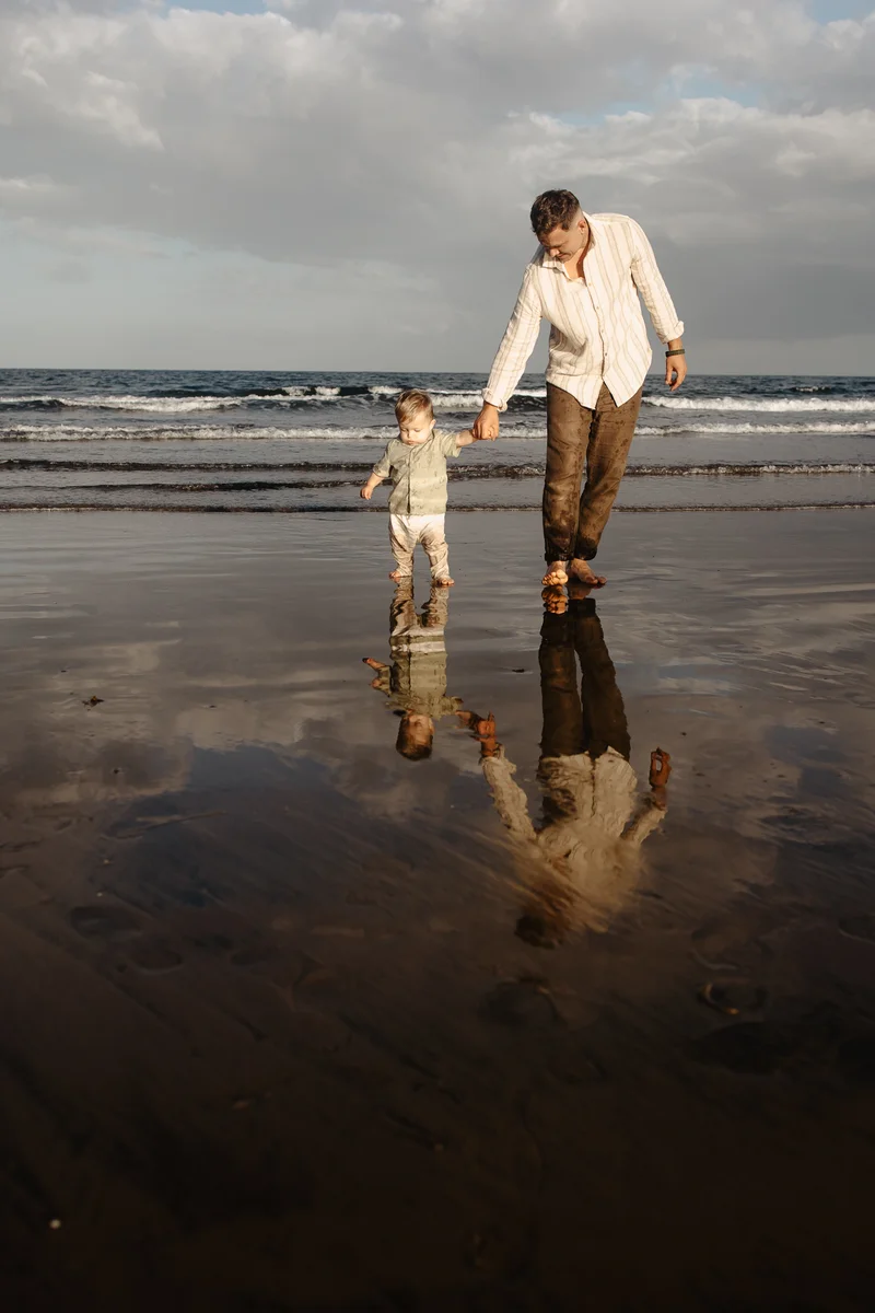 Padre e hijo caminando por playa Tenerife sesión familiar vacaciones reflejos agua conexión