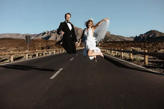 Newlywed couple jumping joyfully on volcanic road Tenerife volcano wedding dramatic landscape backdrop