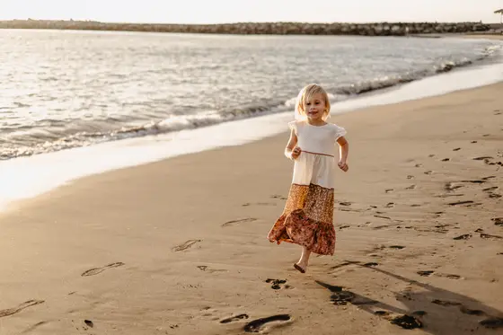 Little girl running on sand during spontaneous play in beach lifestyle session
