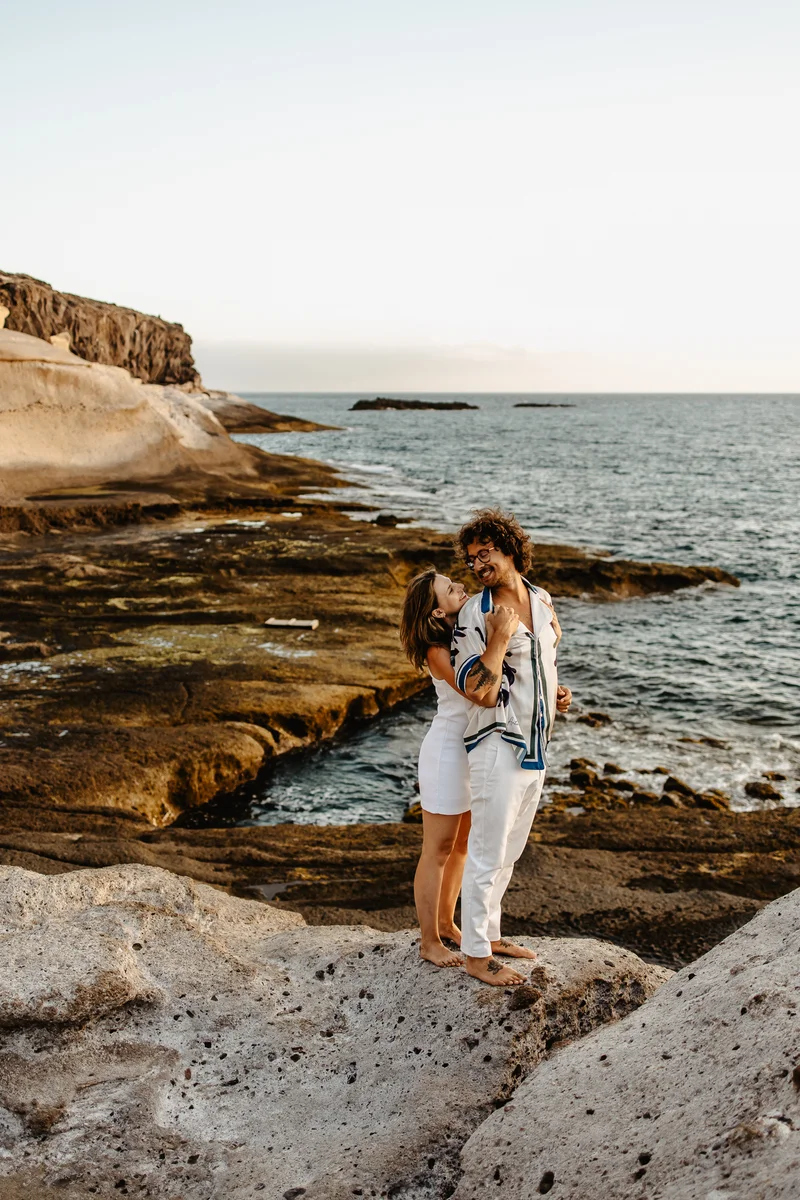 Pareja enamorada abrazándose en acantilados costeros durante fotografía familiar naturaleza en paisaje Tenerife salvaje