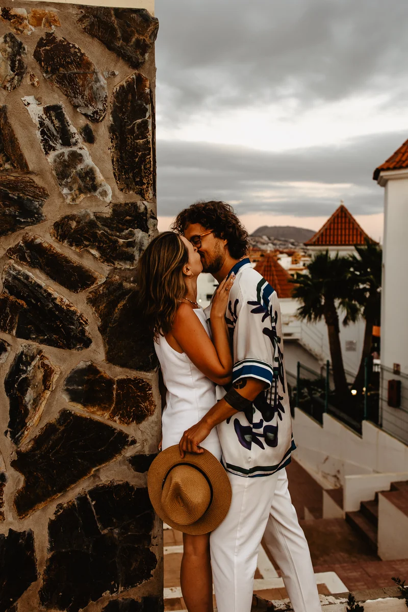 Beso tierno pareja junto pared piedra durante sesión fotografía familiar naturaleza arquitectura tradicional Tenerife