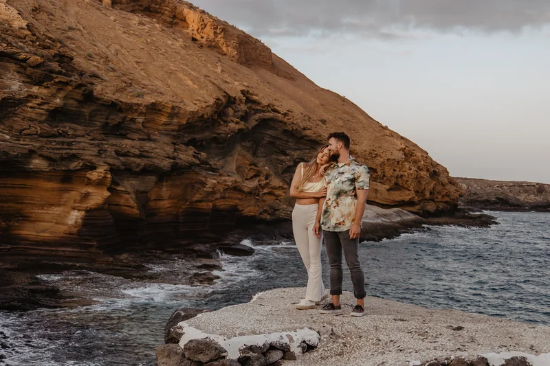 Pareja abrazándose en acantilados con cielo dramático Montaña Amarilla Tenerife sesión fotográfica